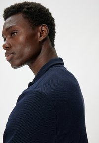 Chaqueta de punto azul marino con cuello alzado, que cuenta con cierre de cremallera. Textura suave, diseño ajustado y costuras en los hombros bien definidas.