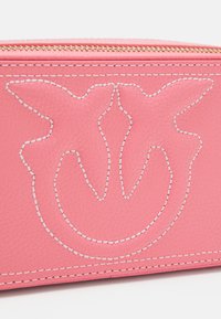 Borsa in pelle rosa con design del logo in rilievo, cuciture bianche e una cerniera dorata nella parte superiore. Texture liscia, forma compatta.