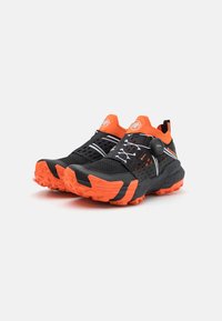 Scarpe da trail nere e arancioni con tomaia testurizzata, sistema di lacci BOA, suola aggressiva e pannelli perforati per la traspirabilità.