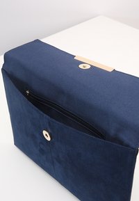 Námořnickou modrou látkovou tašku se zlatým kováním, která má horní uzávěr na patent a vnější zipovou kapsu. Hladká textura a obdélníkový tvar.