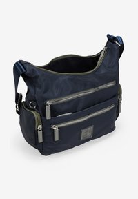 Bolso de hombro de nailon azul marino con múltiples bolsillos con cremallera, acentos verdes, forma rectangular y un parche de logo de marca en la parte frontal.