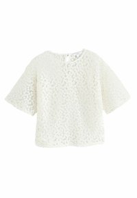 Haut blanc à manches courtes avec un motif floral texturé et un col rond. Il se ferme par des boutons au dos et offre une coupe décontractée.