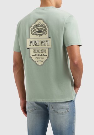 Lichtgroene katoenen t-shirt met een grote grafische afbeelding in crème, tekst "PURE PATH" met een sierlijke bannerontwerp op de achterkant. Casual fit.