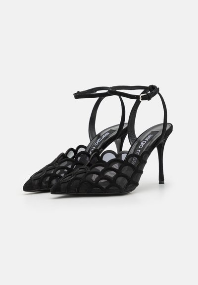 Sandales à talons hauts noires avec un bout pointu et un dessus en maille présentant un design festonné. Sangle de cheville réglable avec fermoir à boucle.