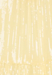 Gul paljetttrikå med en texturerad yta, med vertikala linjer av glittrande paljetter och en rynkad volang i botten.