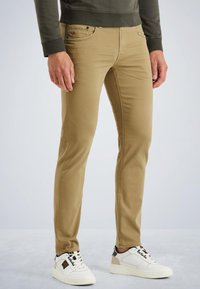 Tan slim-fit chinos made from cotton blend, featuring a smooth texture and front pockets, paired with white sneakers with black accents.