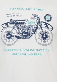 Bílý tričko s modrou grafikou motocyklu a textem "Petrol Industries" a "Hawaiian Kahua Trail" nad a pod ním.