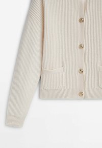 Cream ribbed cardigan with gold buttons, two front pockets, and a boxy shape. Textured fabric with a soft finish.