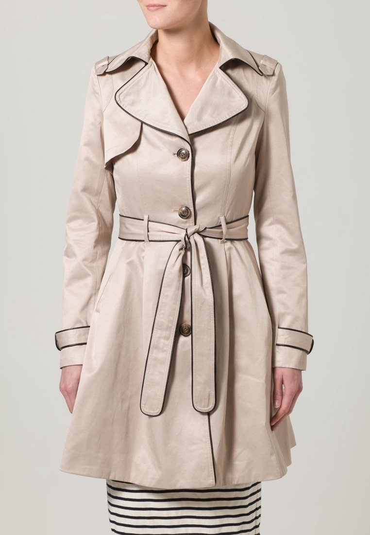 Beżowy trencz wykonany z gładkiej tkaniny, z szerokim kołnierzem, zapinany na guziki, z paskiem w talii oraz czarnymi lamówkami na krawędziach.