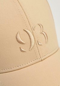 Beżowa czapka baseballowa z haftowanym logo w jasnobrązowym kolorze. Gładka tkanina z widocznymi detalami szycia.