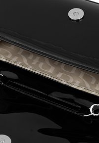 Czarna torebka z lakierowanej skóry o beżowej podszewce z wzorem logo. Srebrne zapięcie na zatrzask i metalowe detale.