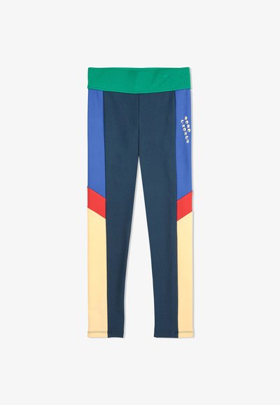 Leggings atletici colorati con un elastico verde a coste. Presentano pannelli blu, blu scuro, rosso e giallo in un design geometrico. Texture liscia.