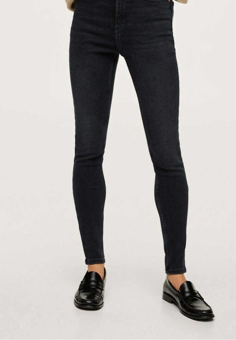 Jeans de mezclilla oscuros y ajustados con una textura suave, cintura alta y corte clásico. Combinados con mocasines negros, que muestran una silueta elegante.