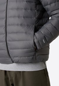 Grå puffjacka med horisontell sömnad, med dragkedjeslutning, sidofickor och elastiska ärmslut. Kännetecknas av sin lätta isolering.