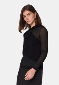 Zwarte hoodie met een geometrisch ontwerp, voorzien van textuur ribbelmouwen en een effen lichaam. Zachte stof met een nette afwerking.