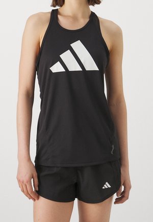Femme portant un haut de sport noir sans manches et un short assorti avec des logos Adidas blancs à l'avant.