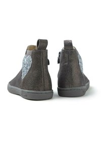 Botines de gamuza gris con un detalle de corazón plateado brillante en el lateral y una suela de goma. Incluyen una pestaña para facilitar su puesta.