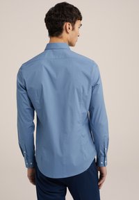 Svetlo modra dolga srajca z ovratnikom na gumb, prirejena za telesno postavo in z usmerjenimi manšetami. Gladka tekstura, zaobljen rob in detajl pri hrbtnem delu.