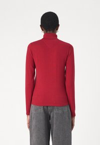 Maglione rosso a maniche lunghe con collo a dolcevita, caratterizzato da una texture a coste e una silhouette aderente. Presenta una sottile cucitura a forma di V sulla parte posteriore.