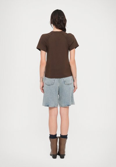 Καφέ κοντομάνικο μπλουζάκι με στρογγυλή λαιμόκοψη, συνδυασμένο με ανοιχτό μπλε denim σορτς. Καφέ μποτάκια μέχρι τον αστράγαλο με μαύρο πλεκτό καλτσοπάπουτσο.