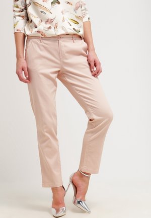 Pantalones rosa pálido hechos de tela suave, con diseño de pierna recta y bolsillos delanteros, combinados con zapatos de tacón metálicos.
