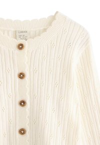 Kremowy sweter kardigan z dzianiny o ryflowanej fakturze, falbaniastym kołnierzyku i małych wzorach w diamenty. Pięć drewnianych guzików z przodu.
