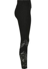 Leggings noirs avec une taille haute et des accents en dentelle sur les côtés inférieurs, mettant en avant un motif floral et une texture lisse.