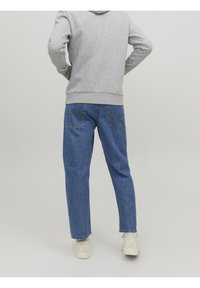 Šedá mikina spojená s modrými džínami z denimu. Džíny mají rovný střih a viditelné švy. Bílé tenisky doplňují vzhled.