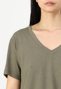 Olive green v-neck t-shirt with short sleeves, made of soft fabric. Features a simple design and a smooth texture.