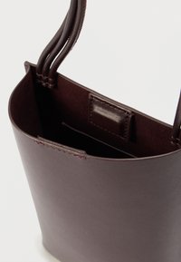 Brown leather handbag with a smooth texture, open top design, and two long handles. Interior features a small patch pocket.