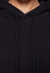 Primo piano di una persona che indossa un hoodie nero con cordini visibili e una cucitura lungo il bordo del cappuccio.