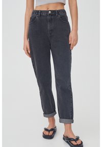 Jean en denim noir taille haute avec ourlets retroussés, cinq poches et fermeture éclair. Le matériau a une finition douce et texturée avec un délavage subtil.