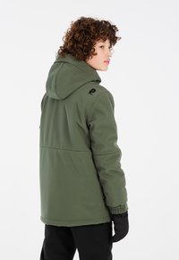 Veste à capuche verte avec des poignets élastiques, une texture lisse, un logo noir sur l'épaule gauche et une silhouette décontractée.