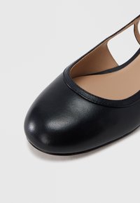 Μαύρο δερμάτινο παπούτσι με στρογγυλεμένη μύτη, επίπεδη σόλα, ανοιχτή φτέρνα και ταμπά εσωτερική επένδυση σε λευκό φόντο.