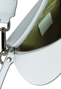 Weißes Lederhandtasche mit silberner Reißverschluss, ausgestattet mit einem gefütterten Innenraum und einer kleinen Tasche. Rundliche Form mit abnehmbarem Tragegurt.