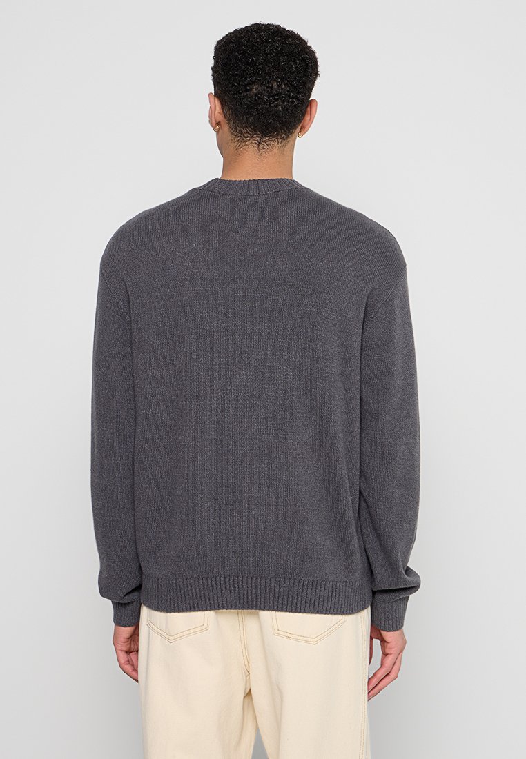 Grauer Strickpullover mit gerippten Bündchen und Saum, mit rundem Halsausschnitt. Der Stoff wirkt strukturiert und weich, entworfen für eine lockere Passform.