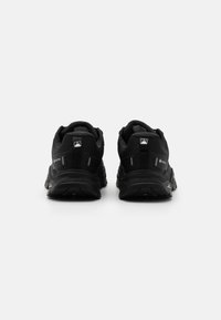 Zapatos de exterior negros con parte superior de tela texturizada, talón reforzado, acentos de logo distintivos y suela de goma resistente. Se muestra la vista trasera.