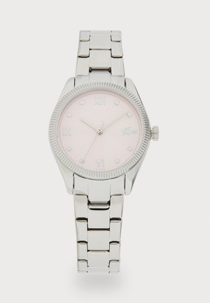 Montre en métal argenté avec un boîtier rond, un cadran rose et des index horaires argentés. Elle présente un bracelet lisse et une lunette texturée.
