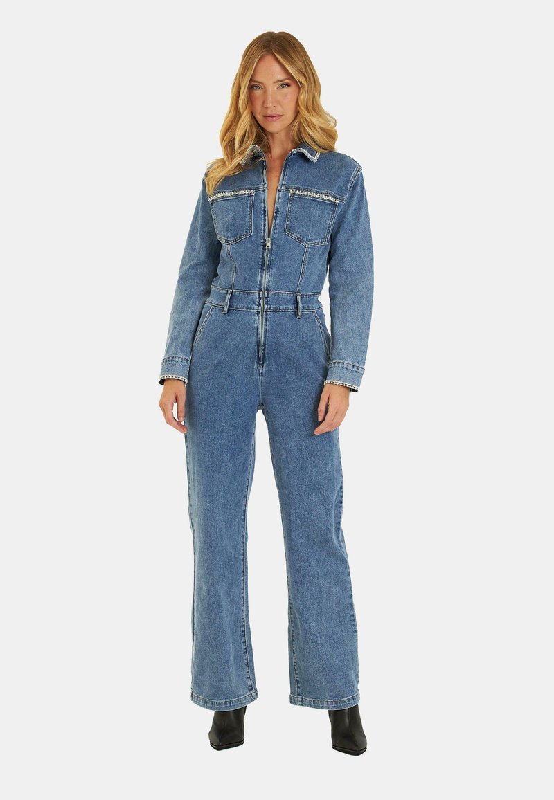 Tuta in denim con maniche lunghe, chiusura frontale con zip, due tasche sul petto e vita affusolata. Colore azzurro chiaro e design a gamba larga. Stivali neri alla caviglia.
