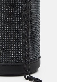 Borsa nera di forma cilindrica, coperta da piccole pietre preziose. Presenta una tracolla in catena nera e una base in pelle texturizzata.