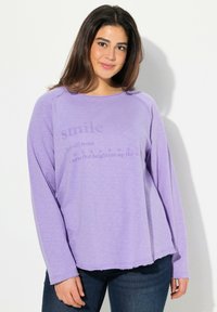 Camicia viola a maniche lunghe con scollo rotondo, che presenta una definizione stampata di "sorriso" sulla parte anteriore. Tessuto leggero e morbido.
