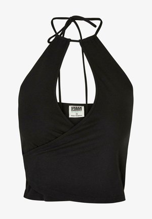 Kobieta ubrana w czarny top na szyję z wycięciem oraz czarne szorty w kwiaty z kieszeniami, do tego czarne sandały na platformie.