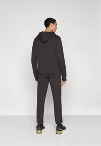 Sweat à capuche gris foncé avec poche kangourou et capuche ajustable, assorti à un pantalon de jogging fuselé de la même couleur et des baskets noires avec des accents verts.