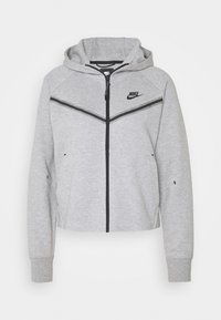 Grå zip-up hoodie med svart dragkedja och detaljer, med huva, raglanärmar och ett chevron-mönster på bröstområdet. Nike-logotypen syns.