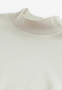 Heledahuline kootud särk heledast beežist puuvilla segust, millel on kõrge krae ja sile tekstuur, minimalistlik disain ning nähtavad mustrid puuduvad.