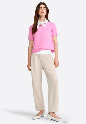 Un haut en tricot rose à manches courtes superposé sur une chemise blanche, associé à un pantalon large beige et des ballerines blanches à bout pointu. Textures lisses, design simple.