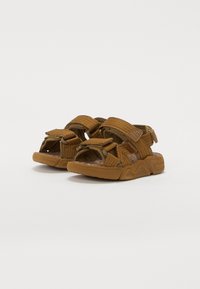 Bruna tygsandaler med justerbara remmar, strukturerad innersula och en solid gummisula. Har en distinkt logotyp på sidan.