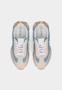 Retro-style Guess-sneakers med beige ruskind og lyseblå denimpaneler, hvide snørebånd og brune rillede såler, set oppefra.