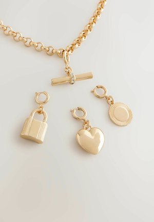 Złoty naszyjnik łańcuszkowy z płaskim centralnym elementem ozdobionym kryształem oraz trzema odczepianymi zawieszkami: kłódką, sercem i promieniami słońca.