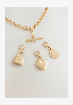 Złoty naszyjnik łańcuszkowy z płaskim centralnym elementem ozdobionym kryształem oraz trzema odczepianymi zawieszkami: kłódką, sercem i promieniami słońca.